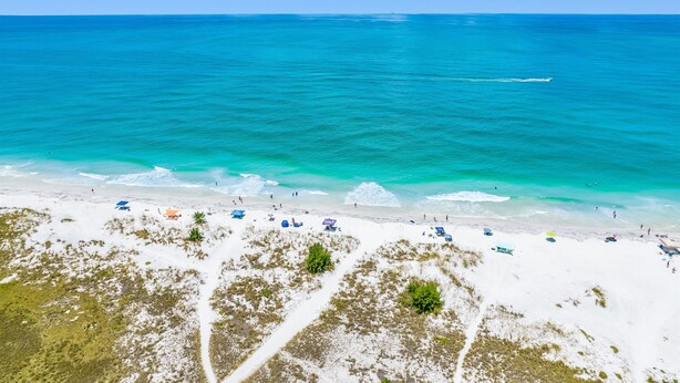 A beach with clear turquoise water, white sand, and several umbrellas and beach chairs. - Paradise Blu by Beach Boutique Rentals (Anna Maria)