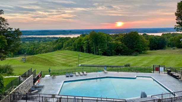 A swimming pool with a view of a sunset over a lake, surrounded by trees and a grassy area.