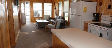 A cabin-style kitchen with wooden walls, a refrigerator, microwave, and a coffee maker.