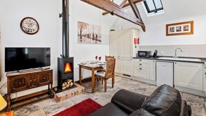 A living room with a fireplace, a television, a sofa, and a kitchen area with cabinets and a microwave. - 1 bedroom accommodation in South Barrow, near Yeovil (South Barrow, near Yeovil)