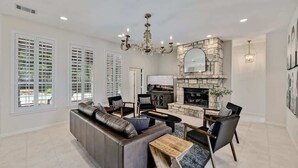 Un salon spacieux avec une cheminée en pierre, un grand canapé et un lustre.