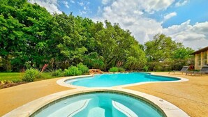 Une piscine au design incurvé, entourée d’une zone sablonneuse et d’une végétation luxuriante.