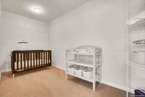 A room with a crib, white shelving unit, and a white storage cart.