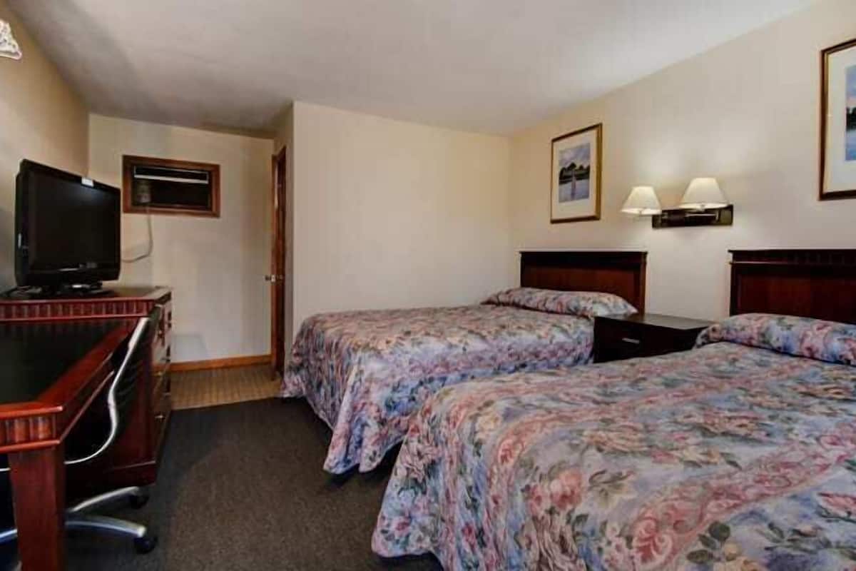 A hotel room with two beds, a desk, a television, and two wall-mounted lamps.
