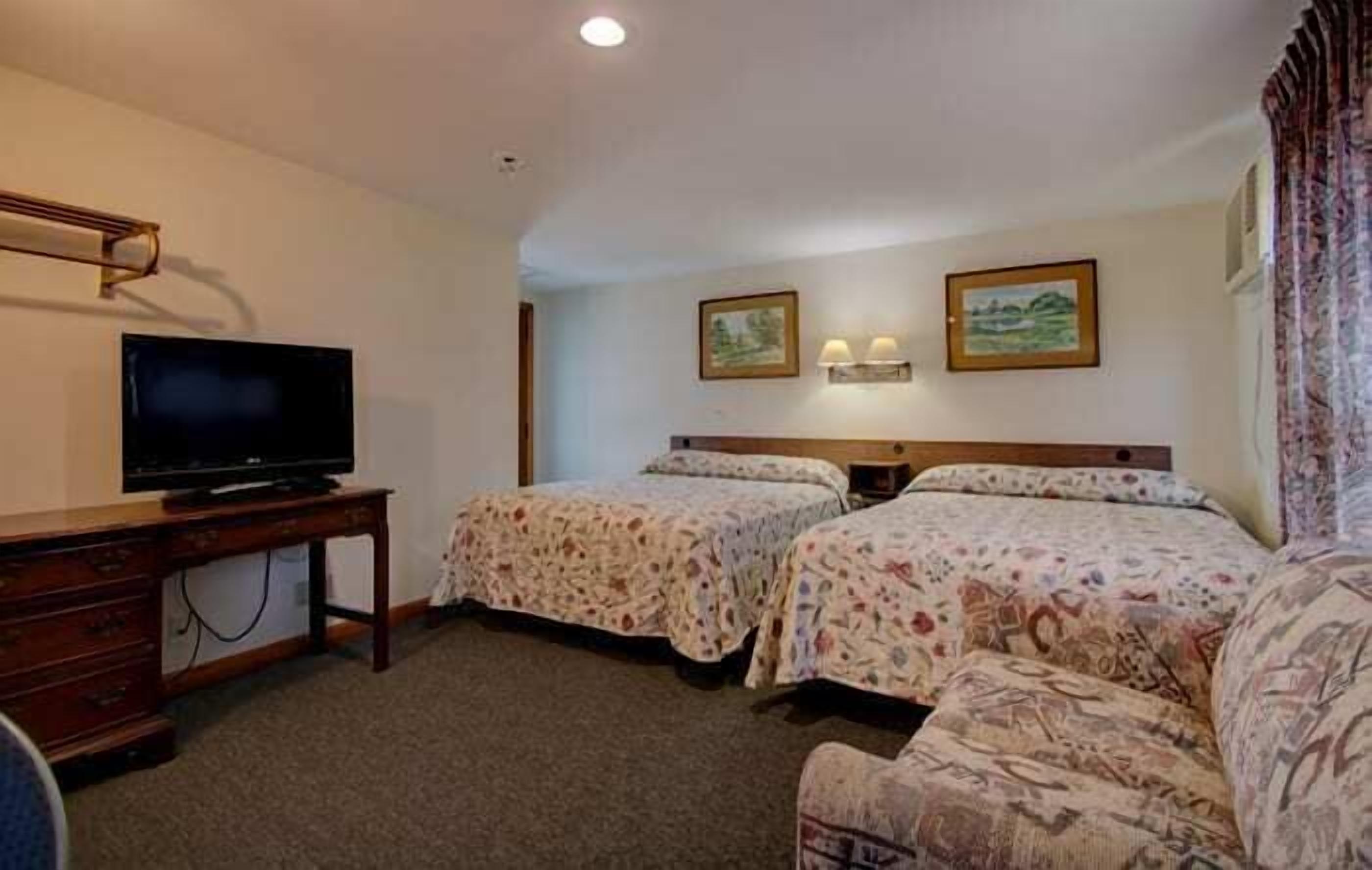 A hotel room with two beds, a TV on a wooden dresser, and two wall-mounted lamps.