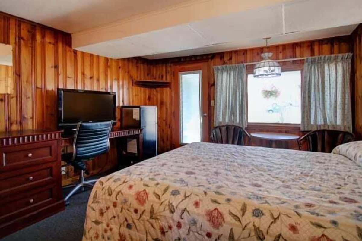 A room with a bed, a desk, a chair, a television, and a window with curtains.