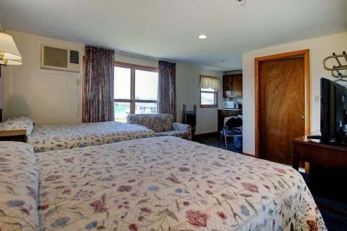 A hotel room with two single beds, a desk, a chair, a television, and a window with curtains.