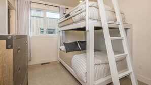 Une chambre avec un lit superposé, une échelle, une fenêtre avec des rideaux et une armoire.