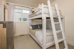 Une chambre avec un lit superposé, une échelle, une fenêtre avec des rideaux et une armoire.