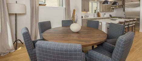 Zona pranzo con un tavolo rotondo in legno circondato da sei sedie imbottite a motivi a scacchi. Sul tavolo è posizionato un vaso grande con rami.