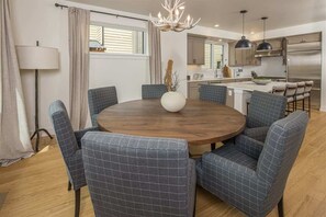 Ein Essbereich mit einem runden Holztisch, um den sechs gepolsterte Stühle mit Karomuster angeordnet sind. Auf dem Tisch steht eine große Vase mit Zweigen.