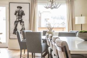 Un espace repas comprenant une grande table et des chaises, un lustre et une œuvre d’art encadrée accrochée au mur.