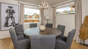 Spiseområde med et rundt bord, seks stole, en lysekrone og en stor vase.
