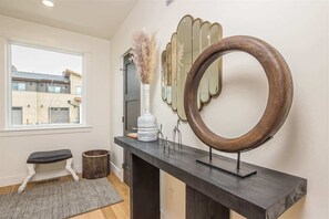 Un couloir avec un banc, un miroir rond et un vase contenant des plantes séchées.