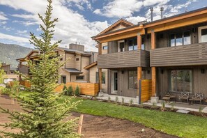 Un immeuble résidentiel moderne avec une façade en bois, de grandes fenêtres et une pelouse bien entretenue.