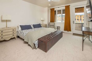 Ein Schlafzimmer mit Bett, Nachttischen, einer Bank, einem Schreibtisch und einem Fenster mit Vorhängen.