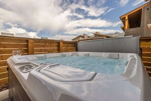 Un bain à remous avec une terrasse en bois et un chalet en bois en arrière-plan.