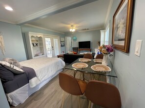 Ein Schlafzimmer mit Bett, Sofa, Esstisch mit Stühlen, Fernseher und einem wandmontierten Spiegel.