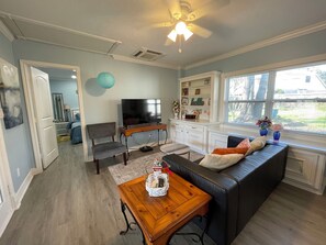 Ein geräumiges Wohnzimmer mit einer dunkelbraunen Ledersofa, einem Holztisch, einem Fernseher und einem Essbereich mit einem weißen Schrank und einem Fenster mit Blick nach außen.