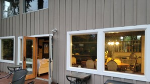 A wooden deck with outdoor seating, a sliding glass door, and a view of the interior dining area. - Riverside Home With a Rustic Charm (Washougal)