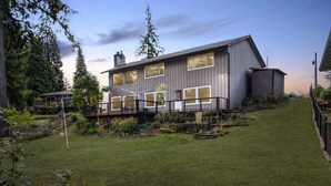 A modern two-story house with a deck, surrounded by a well-maintained garden and tall trees. - Riverside Home With a Rustic Charm (Washougal)