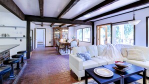A spacious room with a white sofa, a dining table, and a brick floor. - Riverside Home With a Rustic Charm (Washougal)