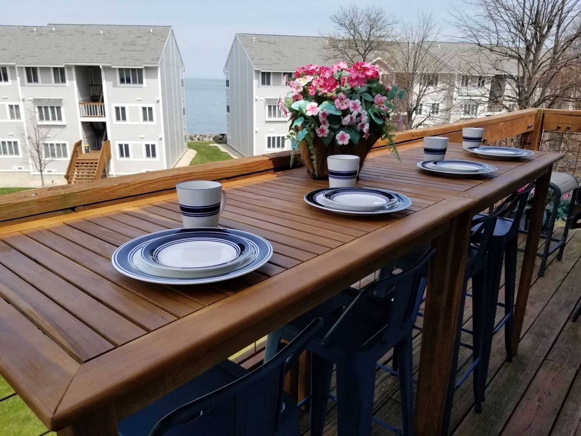 Une terrasse en bois avec une table dressée pour quatre personnes, donnant sur un quartier résidentiel.