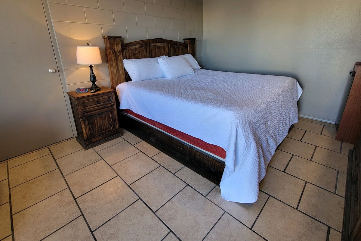 Un dormitorio con una cama, una mesita de noche con lámpara y un cabecero de madera.