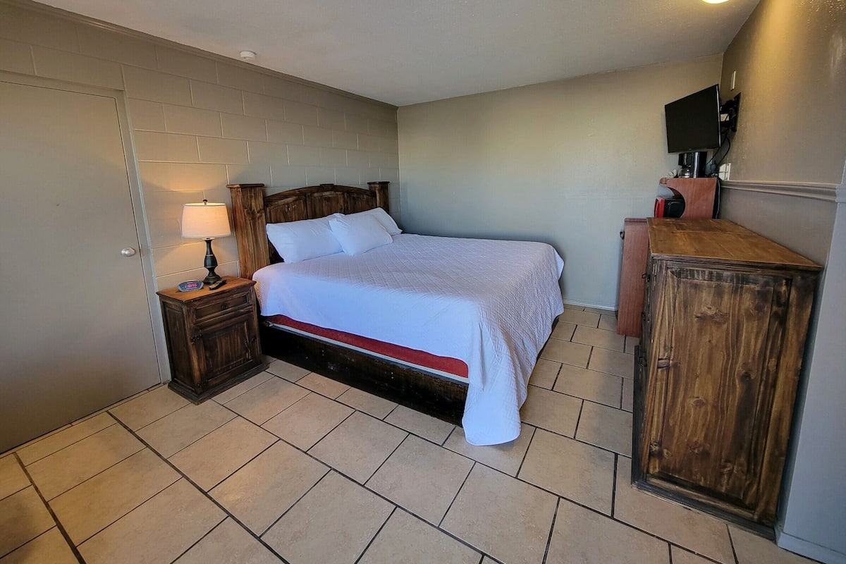 Un dormitorio con una cama de madera, una mesita de noche con lámpara, un armario de madera y un televisor sobre un mueble.