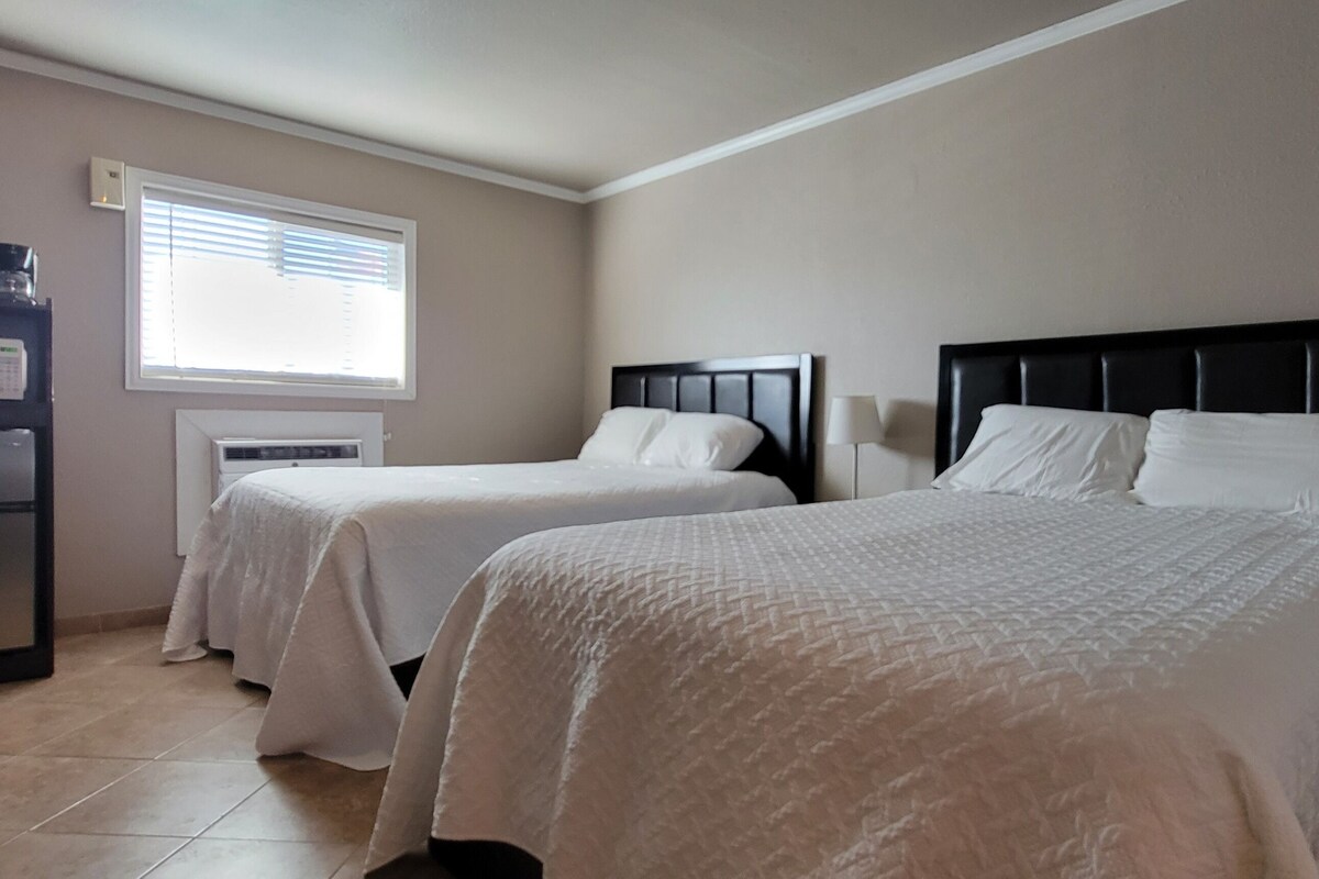 A hotel room with two beds, a microwave, and a window with blinds.