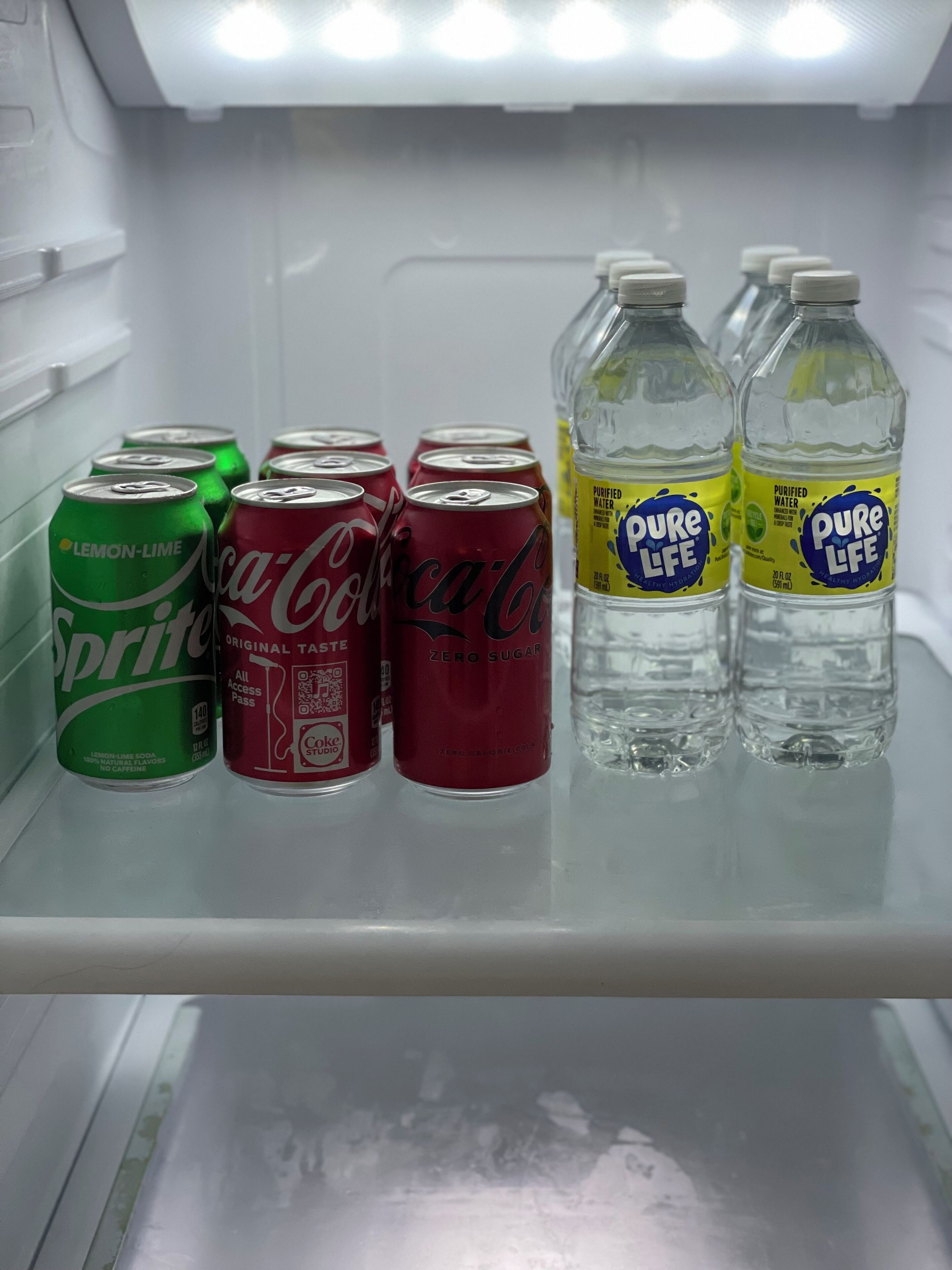 A refrigerator containing various beverages including Sprite, Coca-Cola, and Pure Life water.