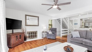 A modern living room with a flat-screen TV, a fireplace, a ceiling fan, and a staircase leading to another level. - Lakefront Retreat at Smith Mountain Lake. Covered Boat Slip + Kayaks (Moneta)