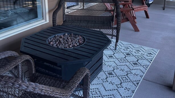 Un patio techado con una mesa redonda, dos sillas de mimbre, una parrilla y vista al jardín trasero.