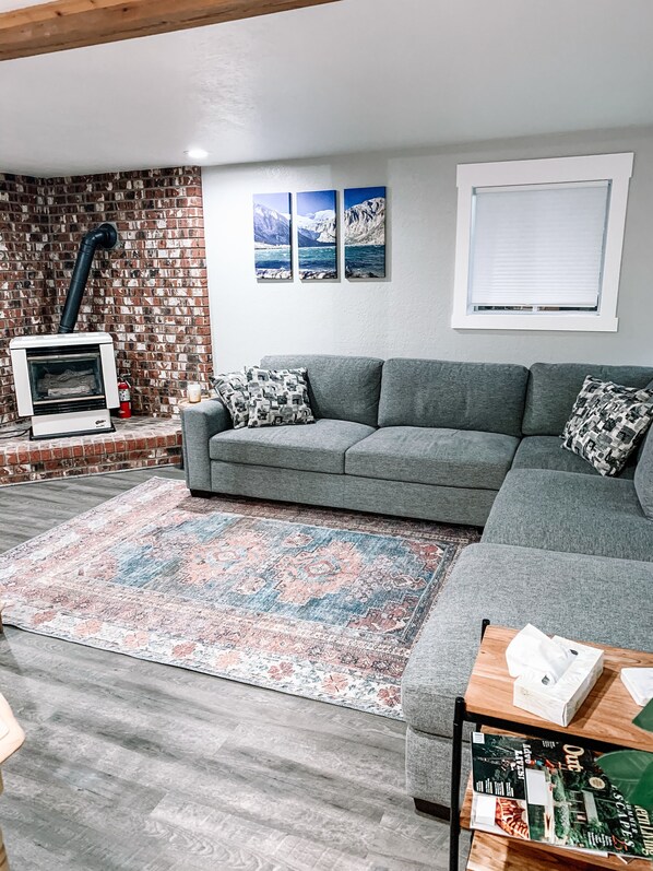 Ein Wohnzimmer mit grauem Sofa, einem gemusterten Teppich und einem Kamin mit Schornstein.