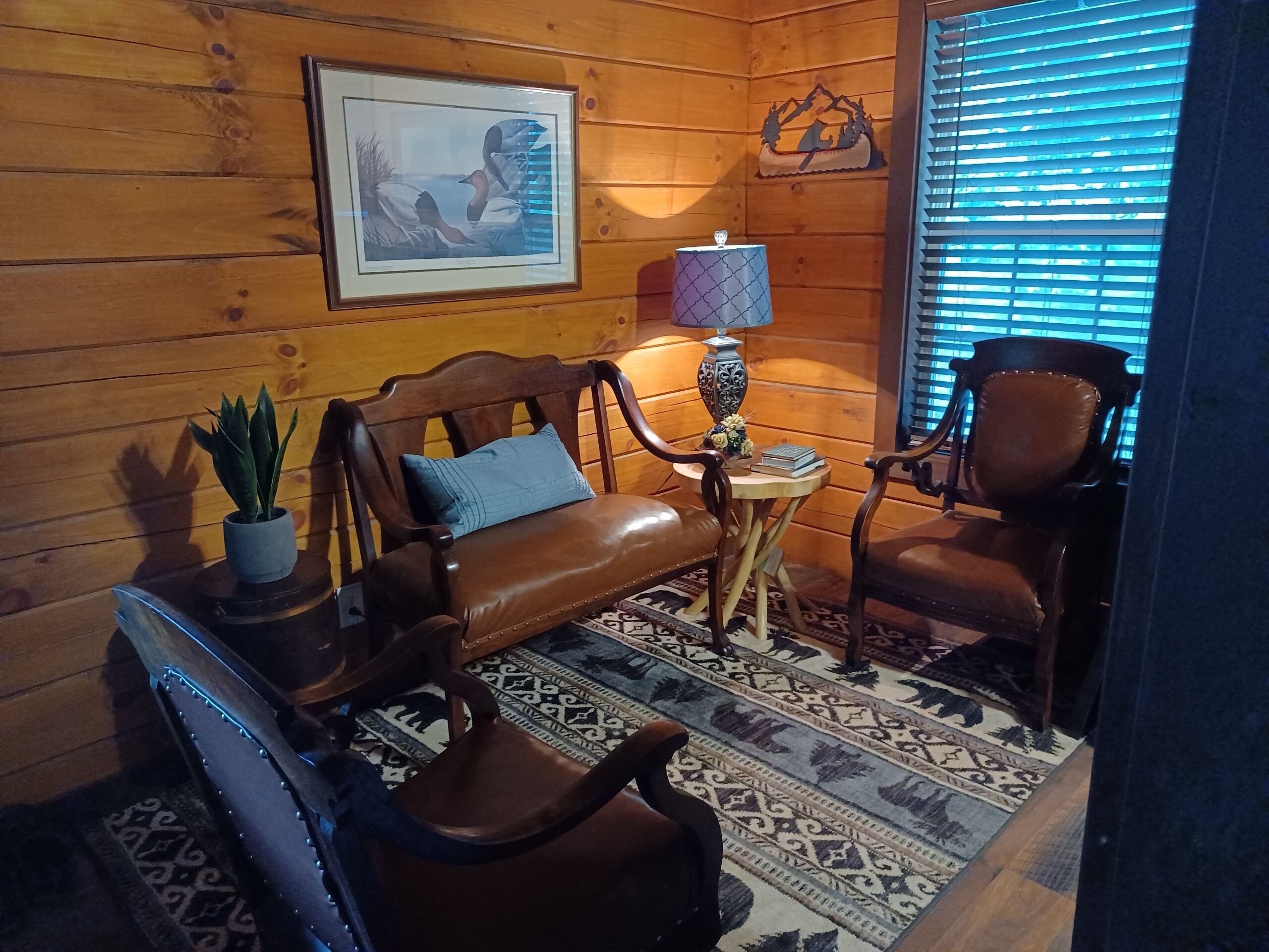A cozy room with a leather sofa, a wooden chair, a small table with a lamp, and a framed picture on the wall.