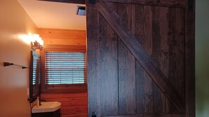 A rustic bathroom with a wooden door, a sink, and a window with blinds. - Bennett Lake Tiny Cabin  (Whitwell)