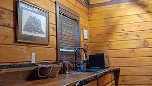 A wooden interior with a kitchen area, including a sink, countertop, and a hanging light fixture. - Bennett Lake Tiny Cabin  (Whitwell)