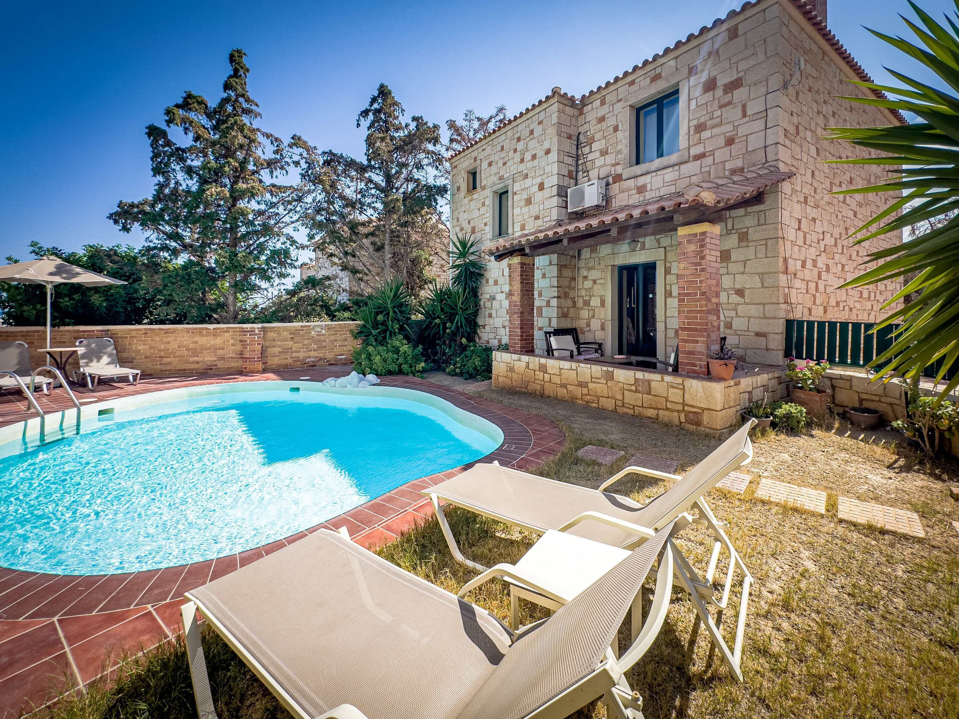 A swimming pool with lounge chairs and a stone building with a tiled roof.