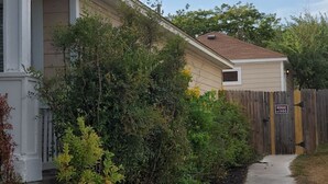 En bostadsfastighet med en gångstig som leder till en grindad entré, omgiven av tät buskvegetation och ett trästaket.