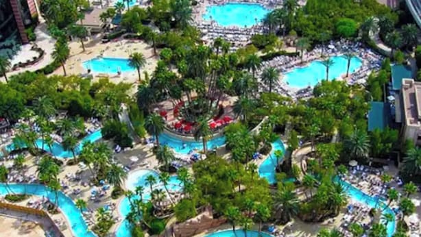 An aerial view of a resort with multiple swimming pools surrounded by palm trees and lounge areas. - MGM Signature 1BR 2BA Wet Republic, Top Golf & Strip Views / NO Resort Fee (Las Vegas)