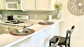 A kitchen with white cabinets, a microwave, a stove, and two bar stools. - Beautiful 2 bed 2 bath Corner Unit with golf course view-5 minutes from beach (Pawleys Island)