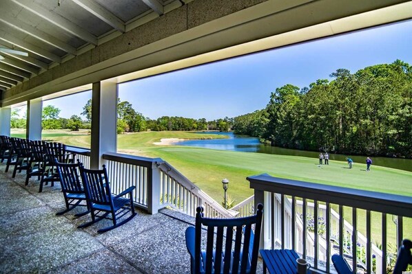 A covered outdoor seating area with chairs and a view of a golf course.
