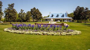 A large building with a blue roof and multiple chimneys, surrounded by a well-maintained lawn and a circular flower bed with purple and white flowers. - Beautiful 2 bed 2 bath Corner Unit with golf course view-5 minutes from beach (Pawleys Island)