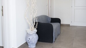 A room with a grey sofa, a white vase with branches, and a tiled floor. - C006 - Camerano, new three-room apartment with garden (Camerano)