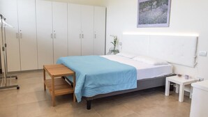 A bedroom with a bed, a bedside table, a nightstand, a wardrobe, and a wall-mounted picture. - C006 - Camerano, new three-room apartment with garden (Camerano)