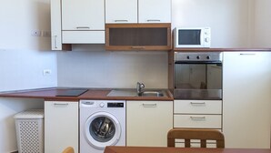 A compact kitchen with a washing machine, microwave, oven, and a wooden table. - C006 - Camerano, new three-room apartment with garden (Camerano)