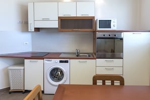 A compact kitchen with a washing machine, microwave, oven, and a wooden table.