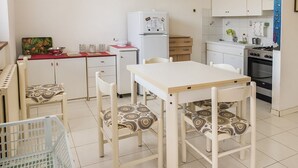 Una piccola cucina accessoriata con frigorifero, fornello e lavandino. Si trova un tavolo da pranzo con sedie e un piccolo armadietto.