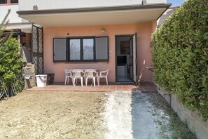 A building with a patio area, a table with chairs, and a door leading to an interior space. - M323 - Marcelli, delightful three-room apartment with garden (Marcelli)