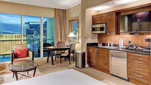Habitación de hotel con balcón, comedor, cocina y televisor grande.